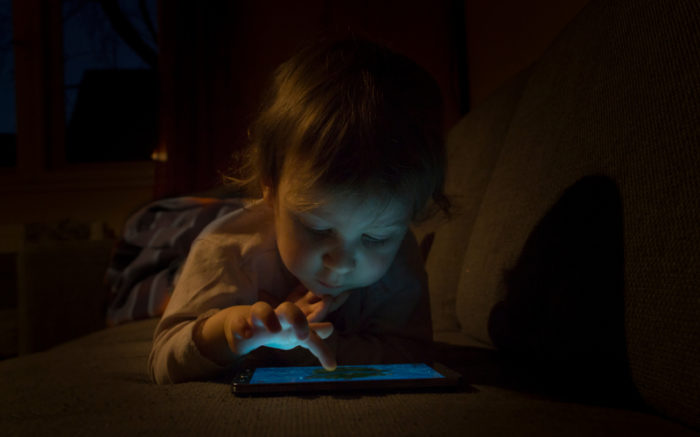 Ein Kleinkind tippt im Dunkeln auf einem erleuchtetetn Tablet.