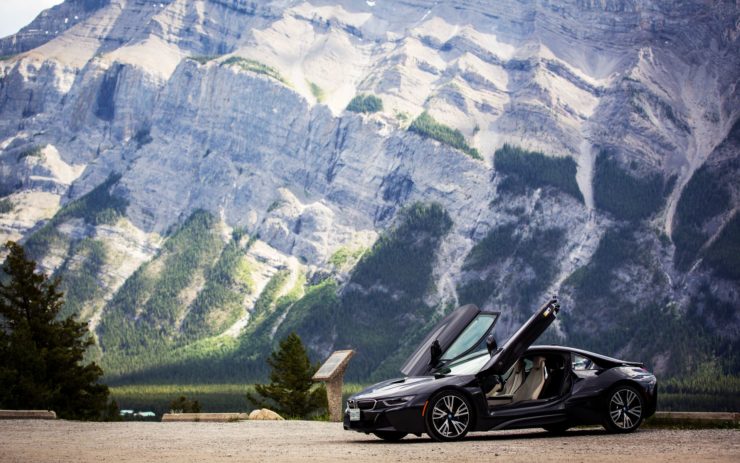 Ein schwarzer glänzender BMW mit aufgeklappten Türen vor Bergkulisse.