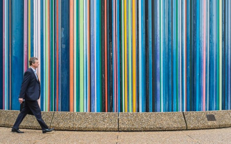 Mann mit Anzug läuft vor farbig gestreifter Wand