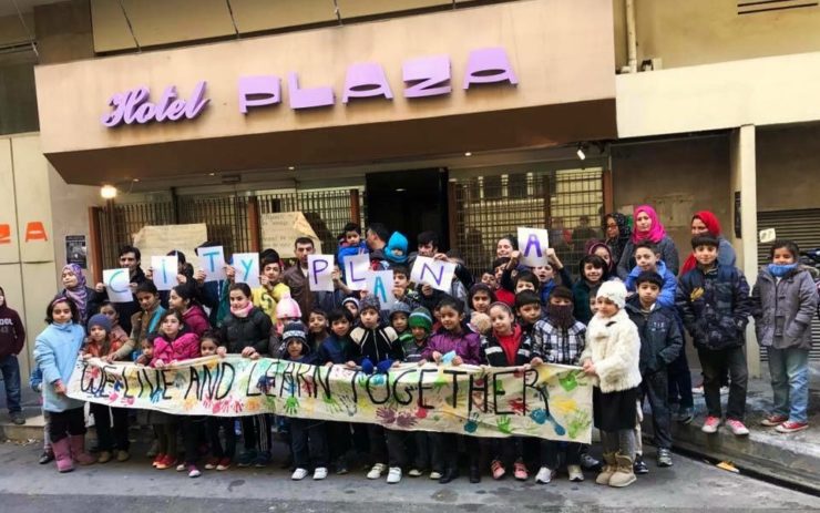 Eine Gruppe Kinder mit Plakat vor dem Eingang des City Plaza Hotels.