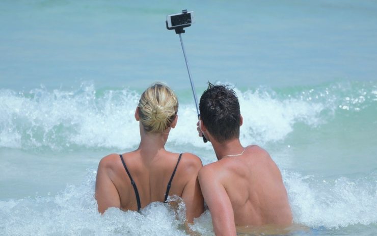 Influencer fotografieren sich mit einem Selfie-Stick am Strand in den Wellen