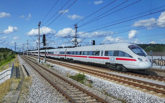 In den Neunzigern wurde die Deutsche Bahn privatisiert - Ist das der Neoliberalismus? Ein ICE-Zug fährt bei schönem Wetter über Gleise.