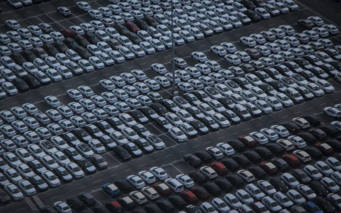 Die Klimakrise wird auch durch das Auto ausgelöst: Auf einem Parkplatz stehen viele weiße Autos, nur wenige Plätze sind frei.