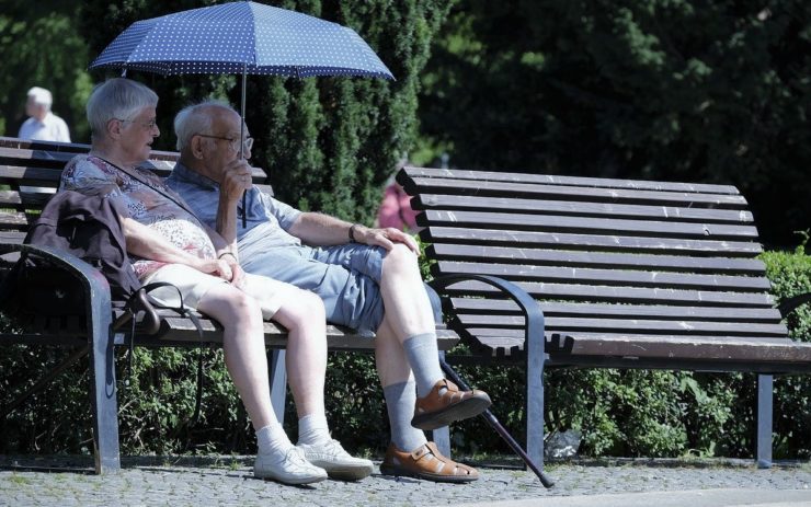 Zwei Renter:innen sitzen auf einer Bank im Park, neben ihnen ist noch eine freie Bank.