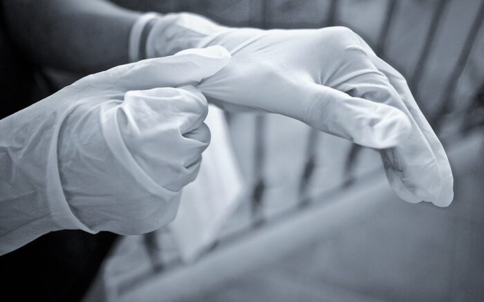Die Hände einer Person, die sich gerade Einmal-Handschuhe anzieht