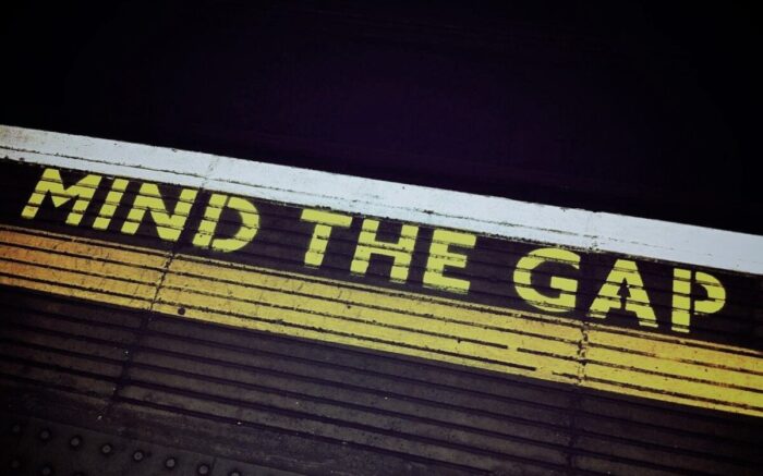 Auf einem Bahnsteigboden steht in gelben Buchstaben "Mind the gap"