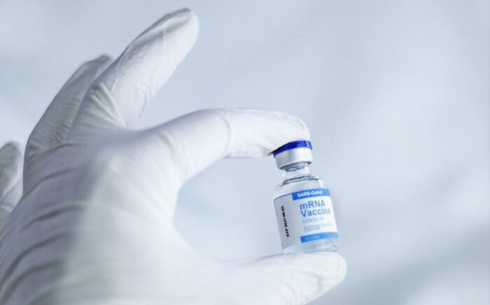 Eine Hand mit Labor-Handschuhen hält eine Dosis Corona-Impfstoff zwischen Daumen und Zeigefinger