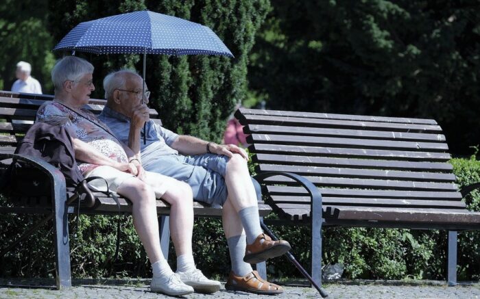 Zwei Menschen in der Rente sitzen auf einer Parkbank mit einem Sonnenschirm