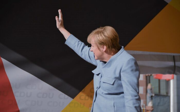 Angela Merkel winkt jemandem außerhalb des Bildes. Sie steht auf einer Bühne, im Hintergrund sind die Farben der CDU und das Logo der Partei zu sehen.