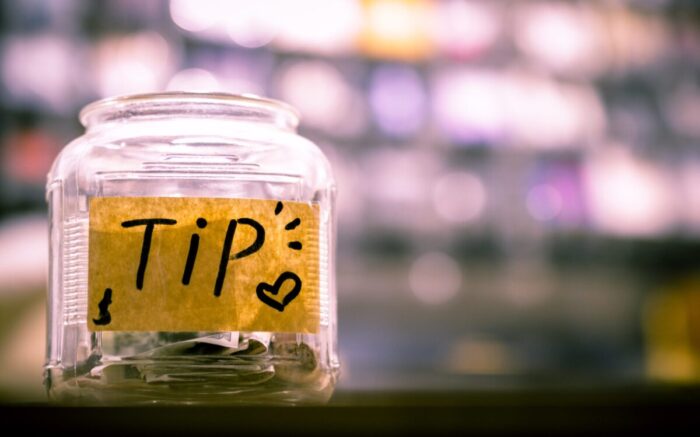 Auf einem Glas mit Kleingeld steht "Tip" (Deutsch: Trinkgeld)