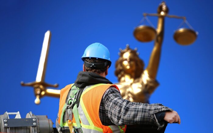 Ein Bauarbeiter auf einer Hebebühne seht vor einer goldenen Justitia im Hintergrund
