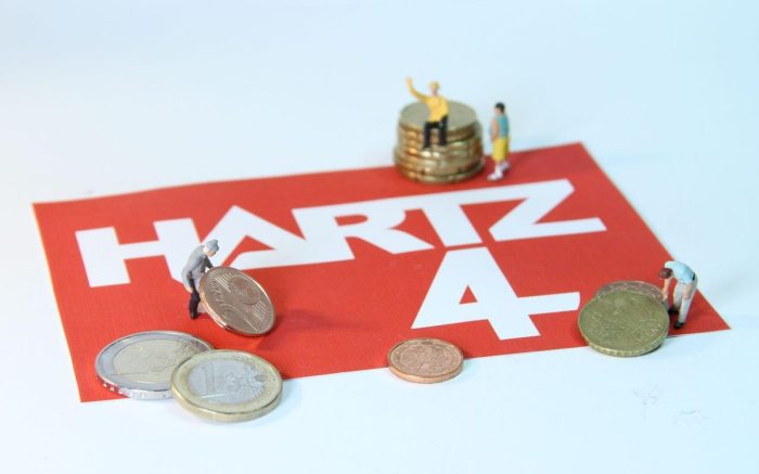Auf dem Schriftzug Hartz 4 spielen Spielfiguren mit Münzen in Wert den Mindestlohn