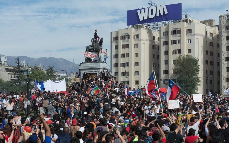 Demonstrant:innen erklimmen nicht Chile-Fahnen und Protest-Schildern eine Statur