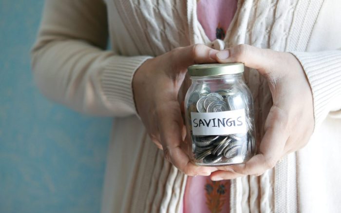 Eine Person mit altmodischer Kleidung hält ein Glas mit der Aufschrift "Savings" in der Hand