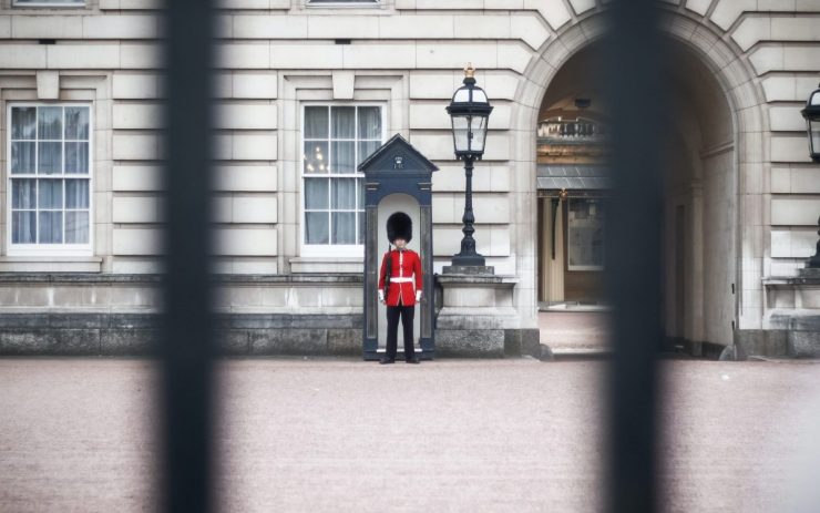Vor dem Buckingham Palace in Großbritannien steht eine typische Wache. Das Bild ist durchkreuz von Gitterstäben