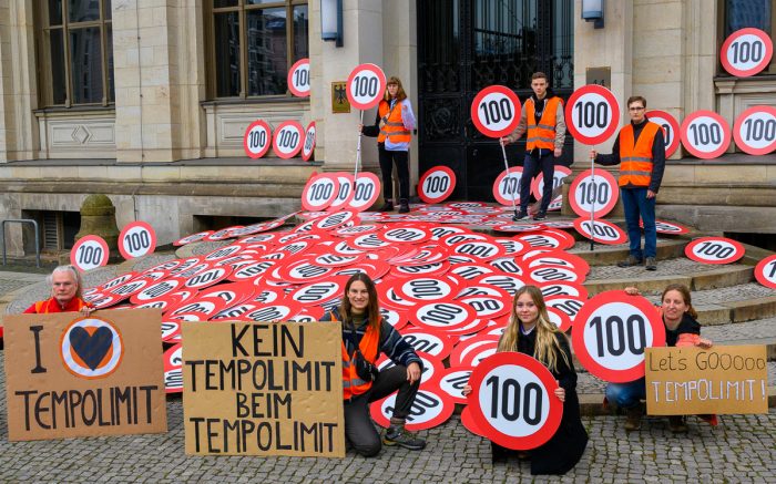 Aktivisten von Letzte Generation bringen Tempo 100 Schilder zum Verkehrministerium. Es werden Demopappen ins Bild gehalten, welche ein Tempolimit von 100 fordern.
